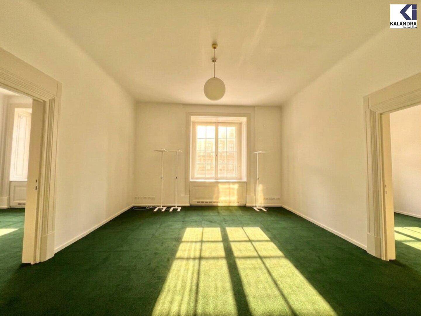 Geräumiger Raum mit leuchtend grünem Teppichboden, hohen Decken und einem großen Fenster, das viel Licht hereinlässt.