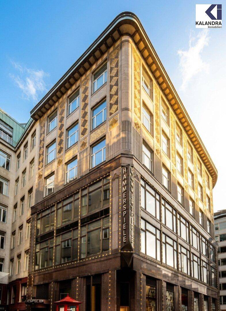Historisches Eckgebäude mit beeindruckender Architektur und großen Fenstern an einer sonnigen Stadtkreuzung.
