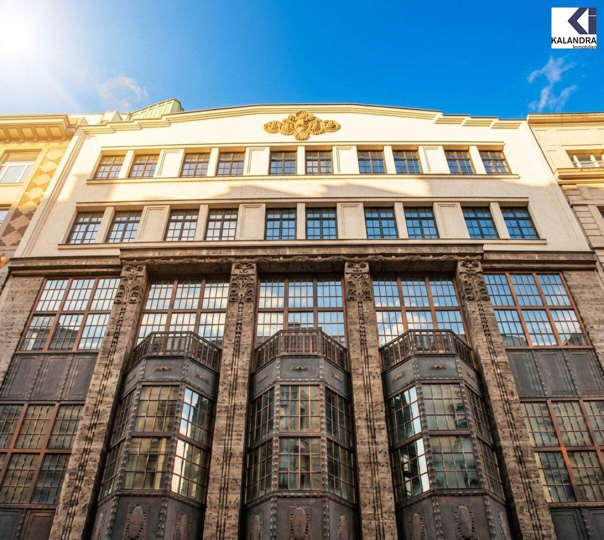 Obere Fassadenansicht eines historischen Gebäudes mit dekorativen Elementen und vielen Fenstern unter blauem Himmel.