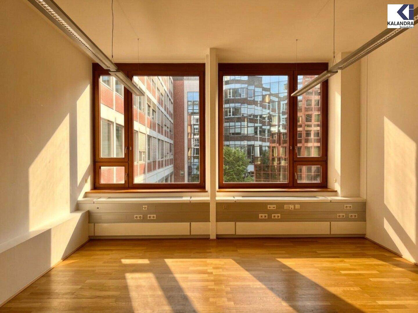Leerer Büroraum mit Holzfenstern und integrierten Ablagen unter den Fenstern, beleuchtet von der Nachmittagssonne.