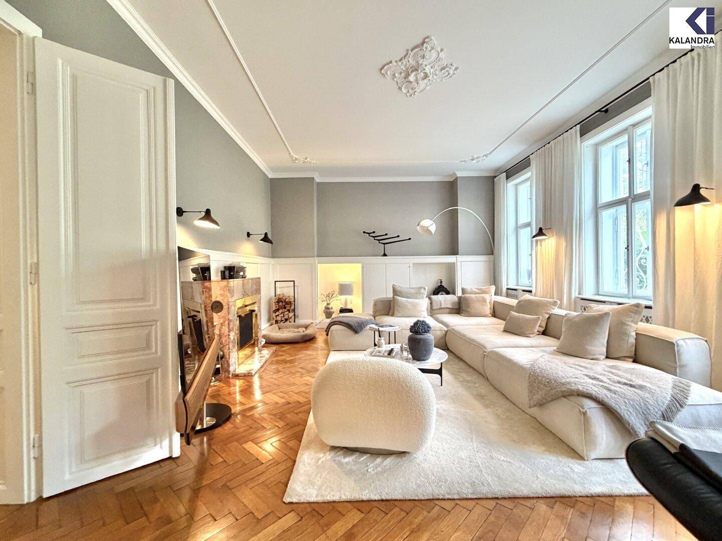 Elegantes Wohnzimmer mit großem Ecksofa, Fischgrätparkett, hohen Decken und einem dekorativen Kamin.