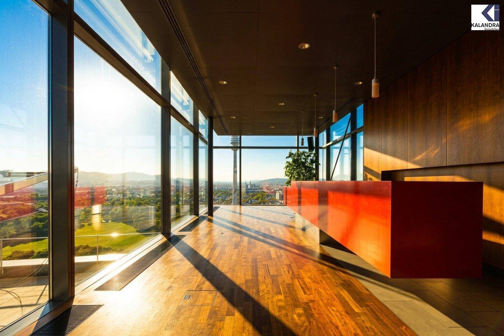 Moderner Empfangsbereich mit auffälliger roter Theke, Holzboden und bodentiefen Fenstern mit Weitblick.