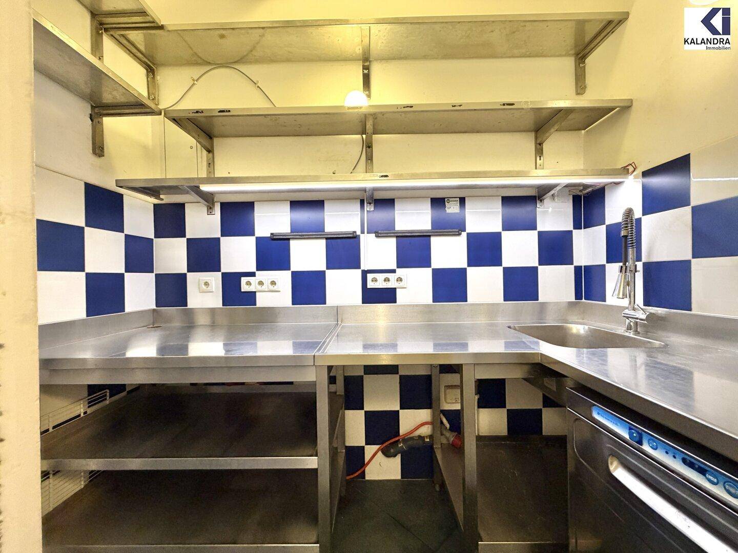 Professionelle Küchenzeile mit Edelstahl-Arbeitsplatten, Spüle und blau-weiß gefliesten Wänden.