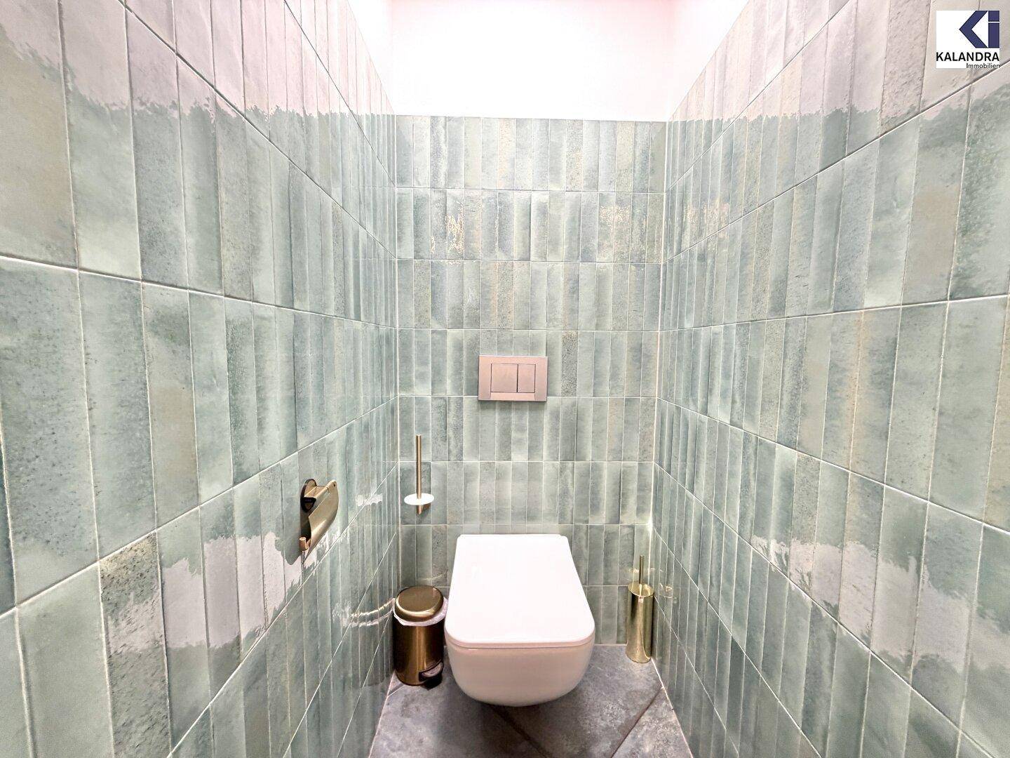 Modernes WC mit wandhängender Toilette und auffälligen grünen Wandfliesen, stilvoll eingerichtet.