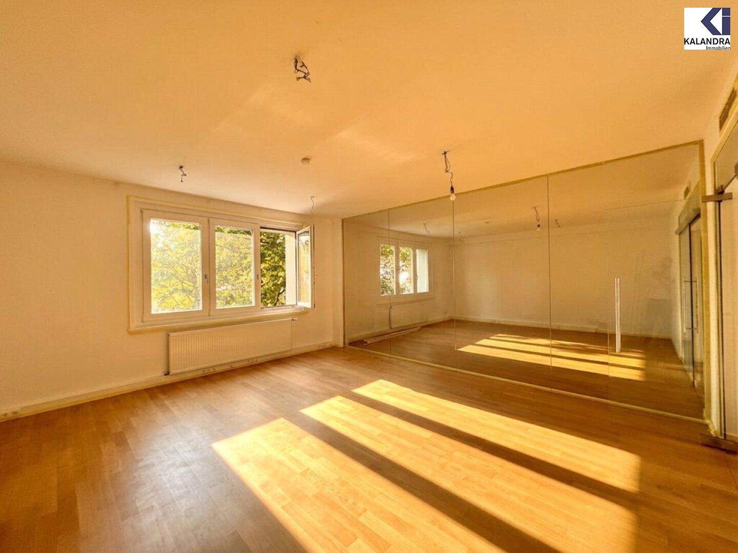 Heller Wohnraum mit Holzboden, großen Fenstern und einer reflektierenden Wand, die den Raum optisch vergrößert.