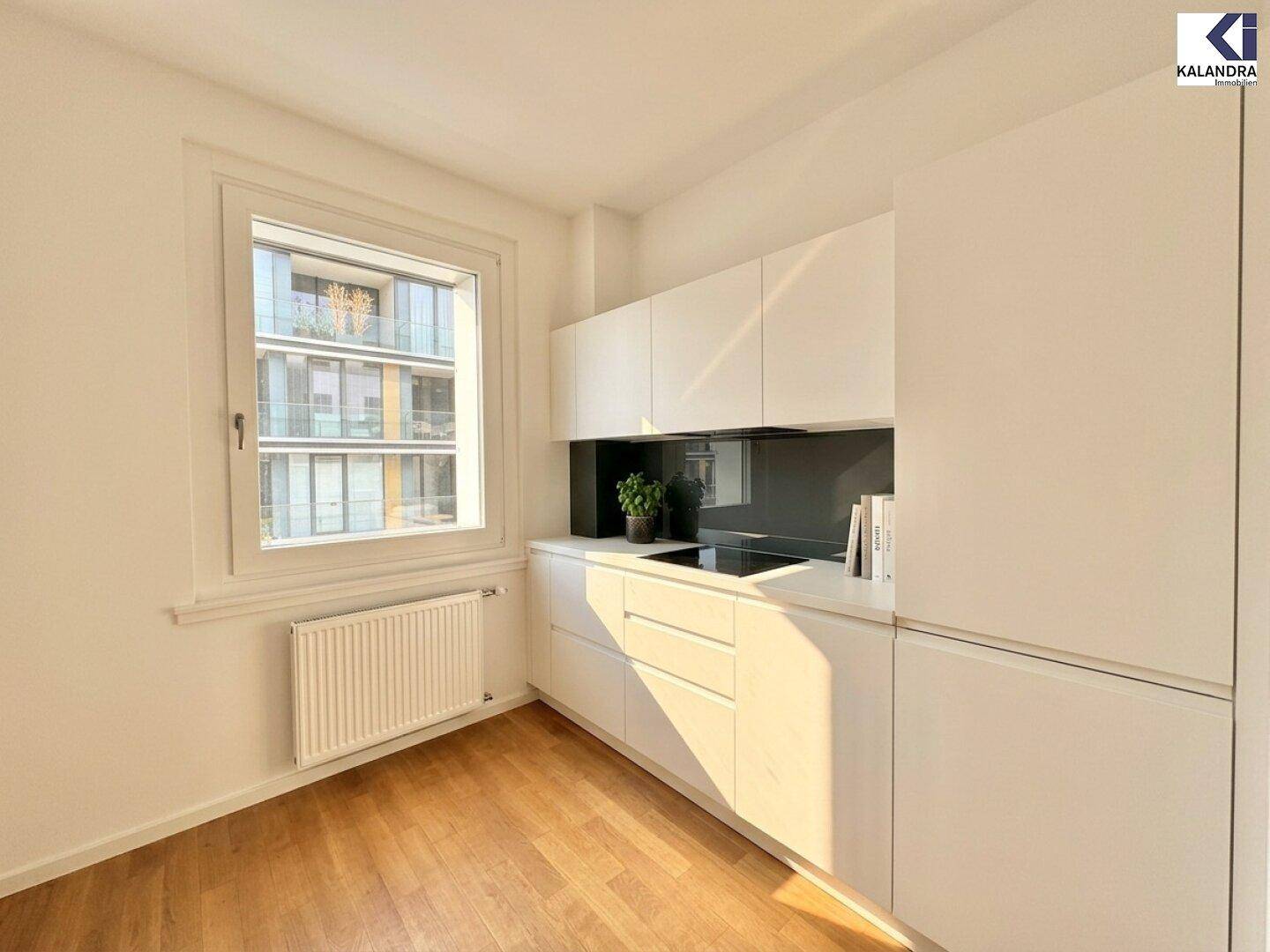 Moderne, weiße Einbauküche mit minimalistischem Design, Induktionskochfeld und Fensterblick.