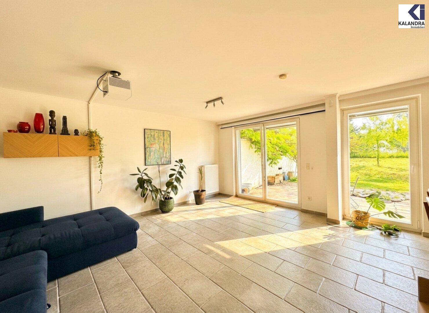 Helles Wohnzimmer mit Fliesenboden und großen Fenstern zum Garten.