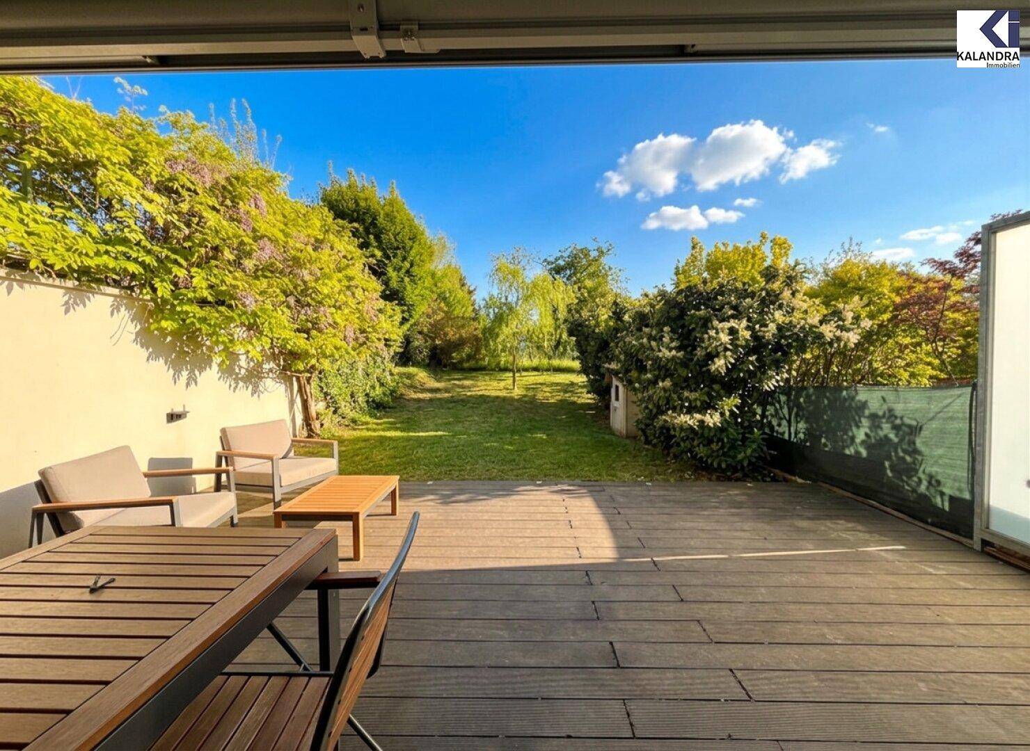 Holzterrasse mit Gartenmöbeln und Blick auf den weitläufigen grünen Garten.