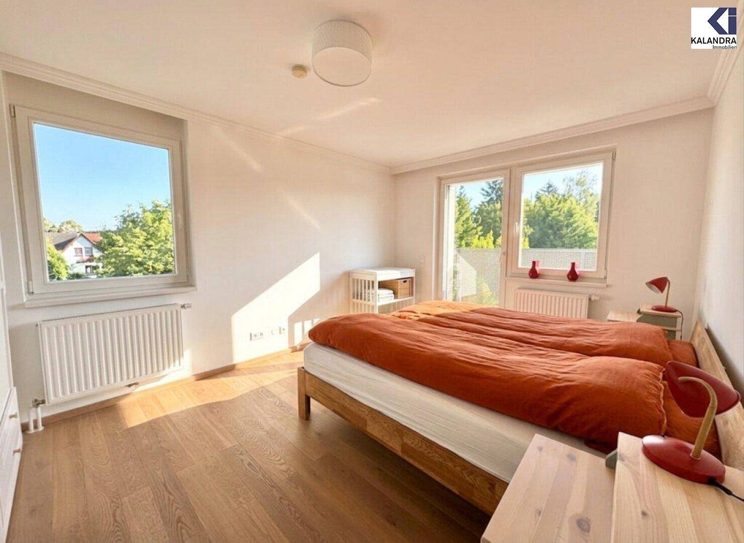 Helles Schlafzimmer mit Holzboden, Doppelbett und Blick ins Grüne.