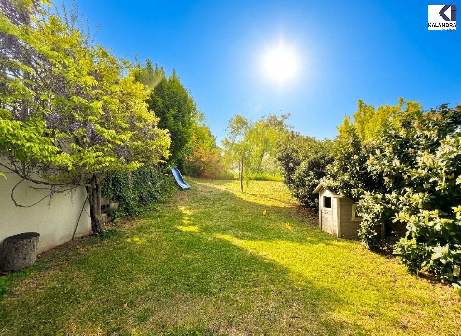 Sonnige Gartenansicht mit Rasen, Bäumen und einer Kinderrutsche.
