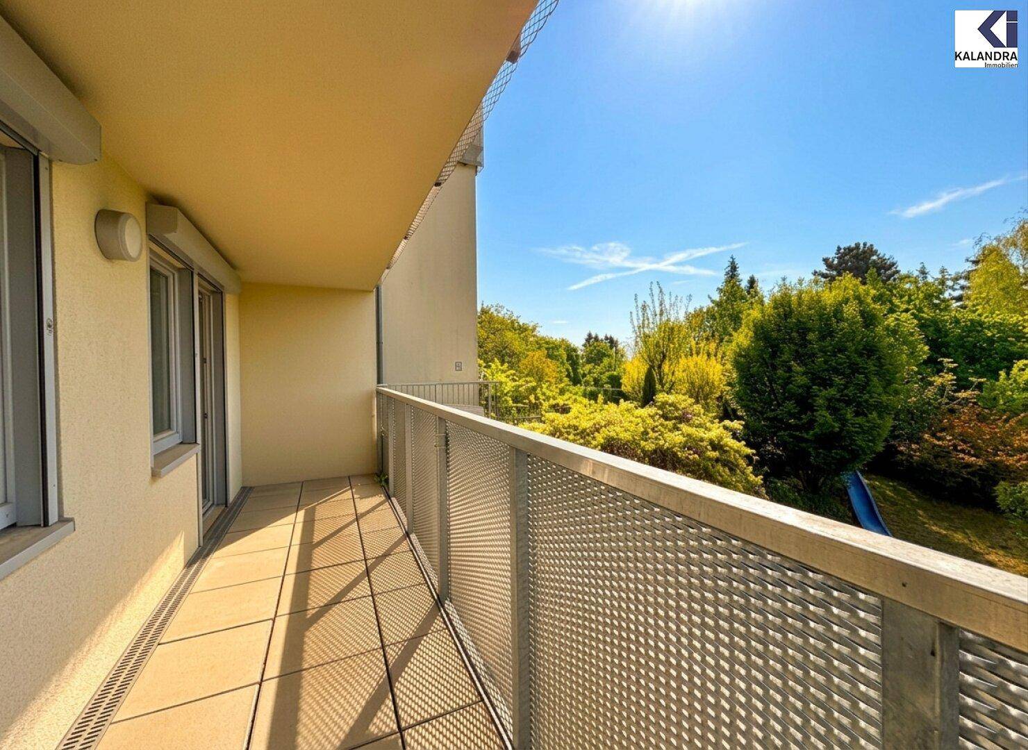 Heller Balkon mit Metallgeländer und sonnigem Ausblick ins Grüne.