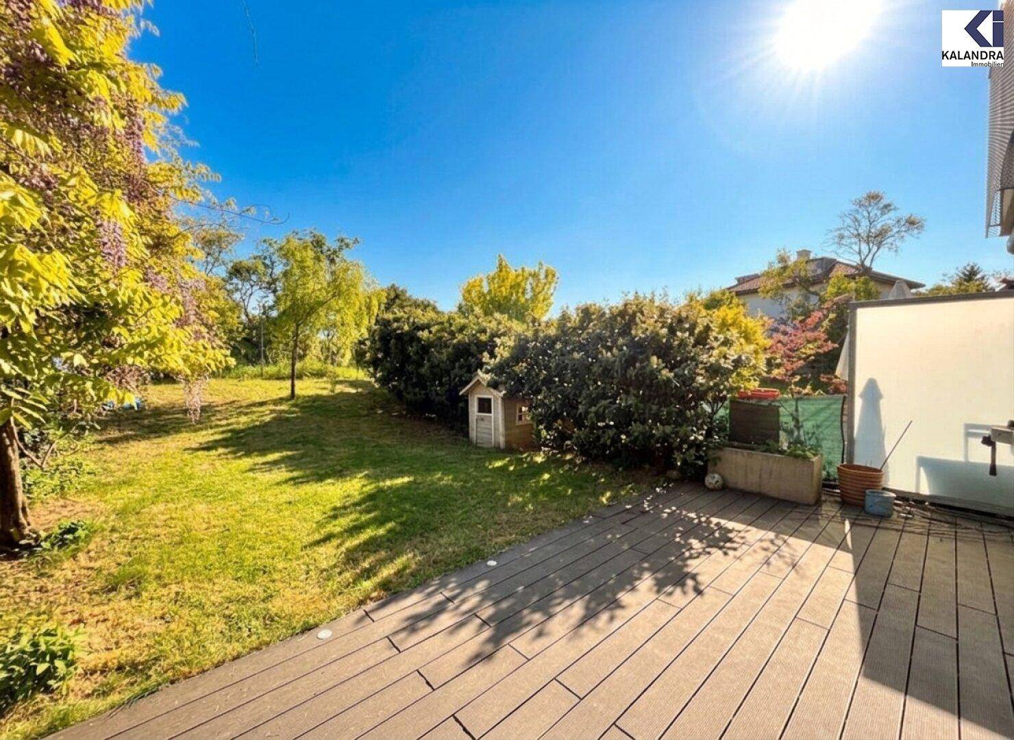 Holzterrasse mit Blick auf den weitläufigen grünen Garten und blühende Sträucher.