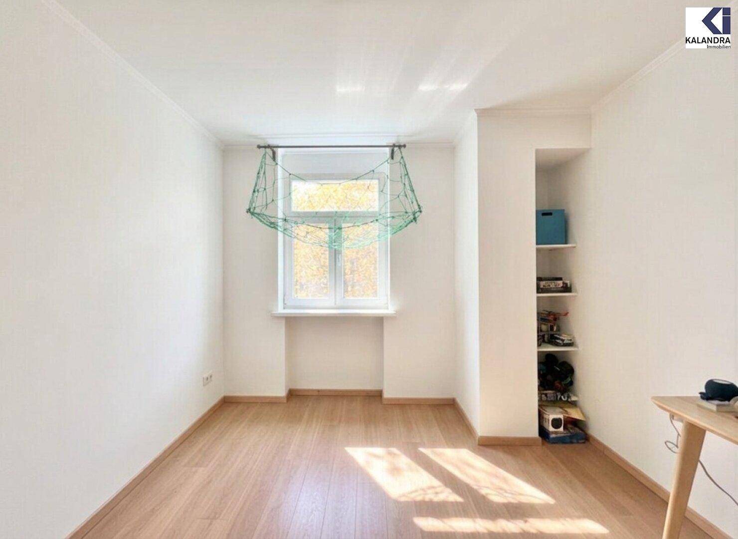 Helles, leeres Zimmer mit Holzboden und Fenster zum Außenbereich.