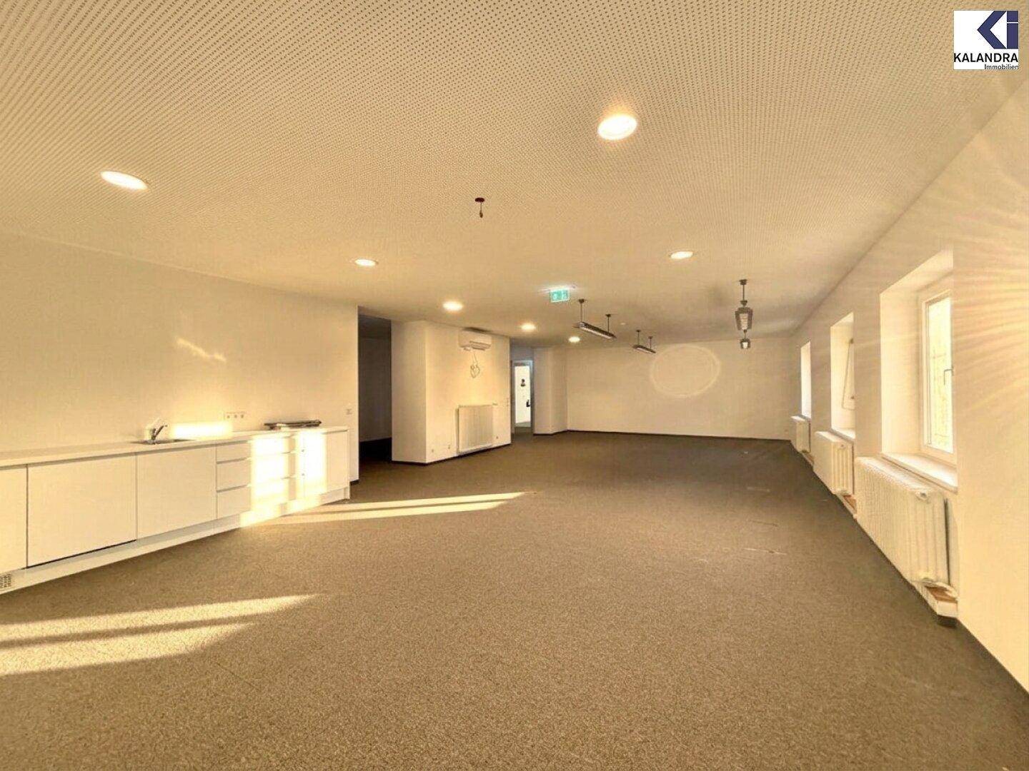 Großer, leerer Büroraum mit Teppichboden, Einbauschränken und natürlichem Lichteinfall durch die Fenster.