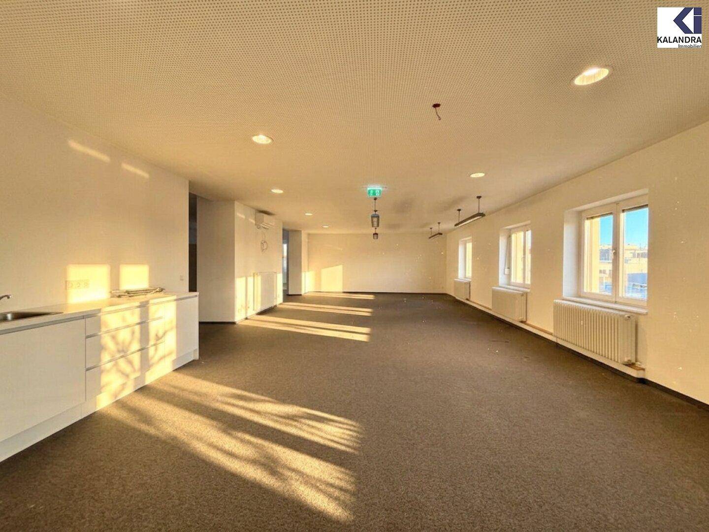 Heller Büroraum mit Teppichboden und Einbauschränken, durchflutet von Sonnenlicht, das lange Schatten wirft.