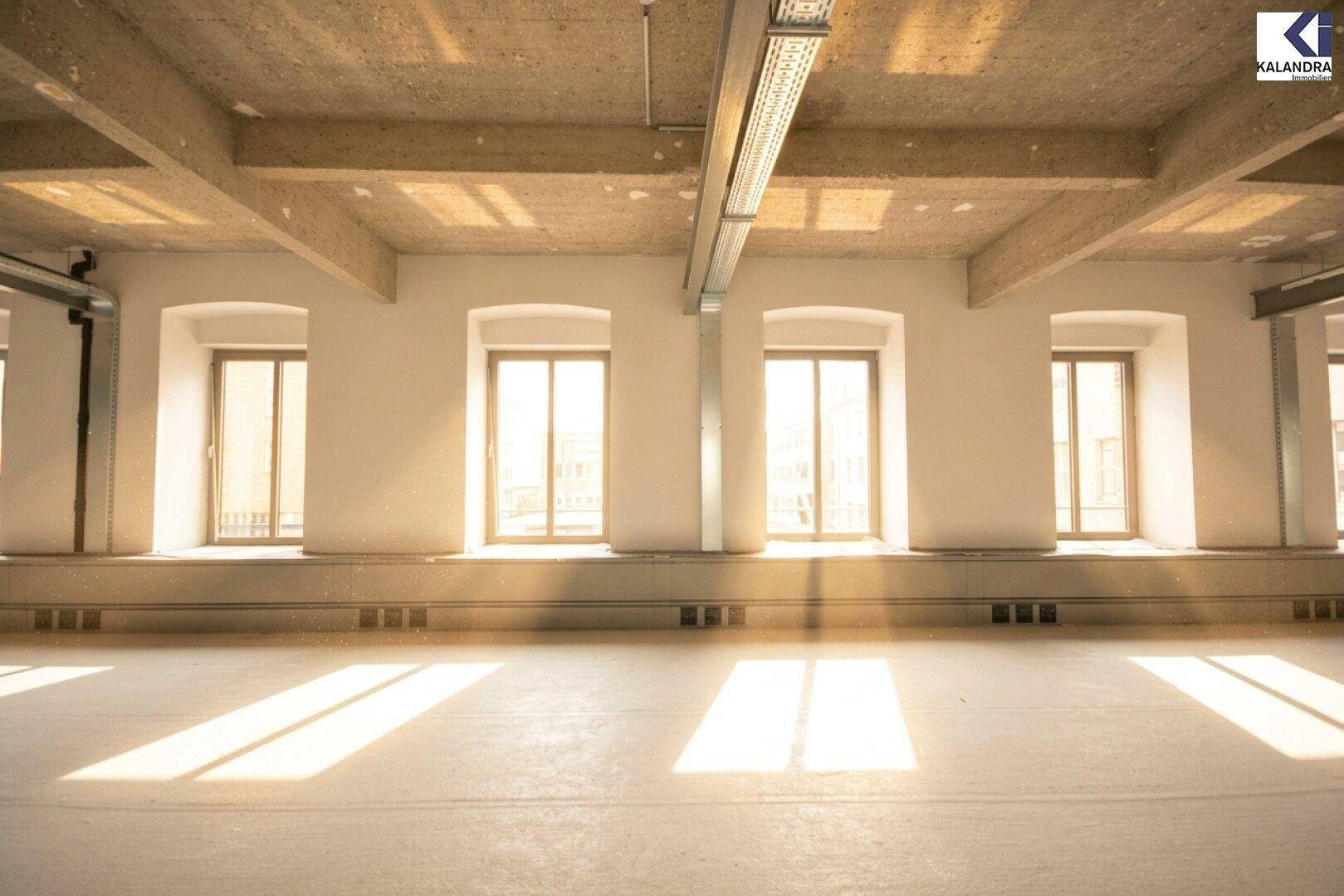 Helle Fensterfront in einem großen Raum mit viel Tageslicht und sichtbaren Deckeninstallationen.