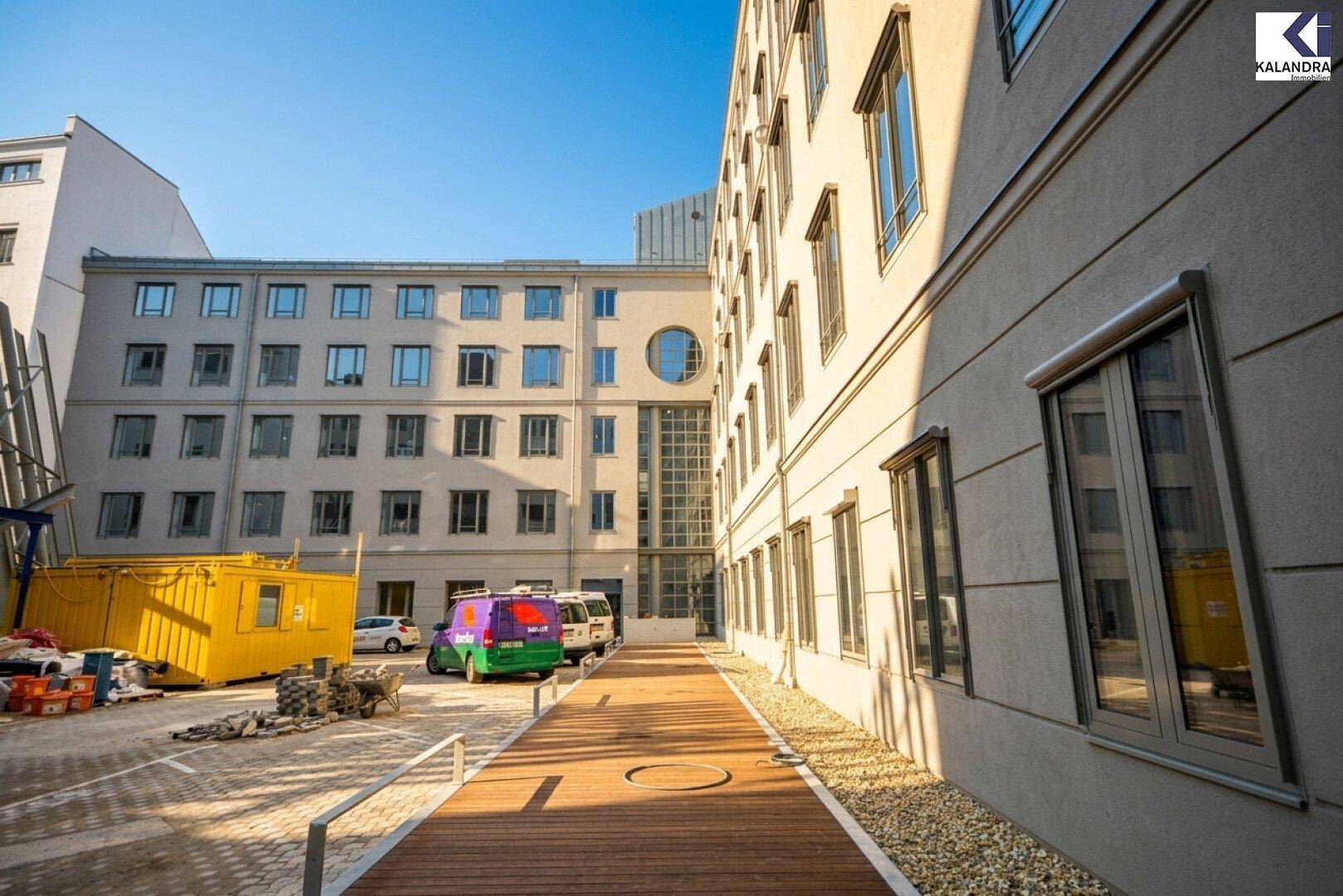 Innenhofbereich zwischen Gebäuden mit Holzweg und geparkten Lieferwagen.