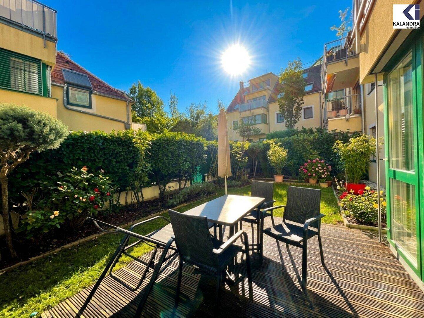 Heller Gartenbereich mit Holzterrasse und Gartenmöbeln unter strahlendem Sonnenschein, umgeben von Grün.