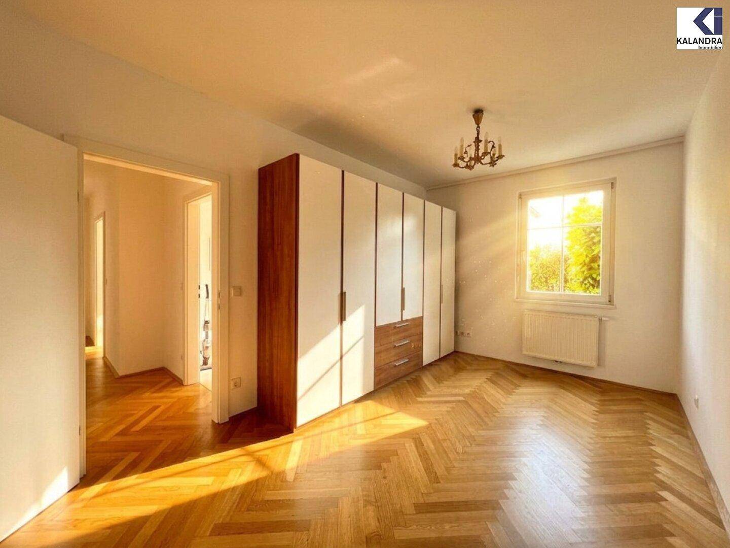 Schlafzimmer mit Fischgrätparkettboden, großem Kleiderschrank und viel natürlichem Licht durch das Fenster.