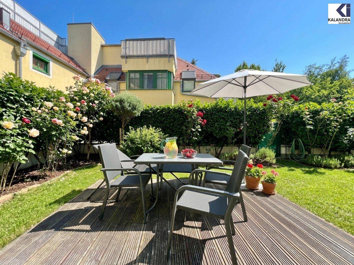 Gepflegter Garten mit Holzterrasse, Esstisch und Stühlen, umgeben von blühenden Rosenbüschen.