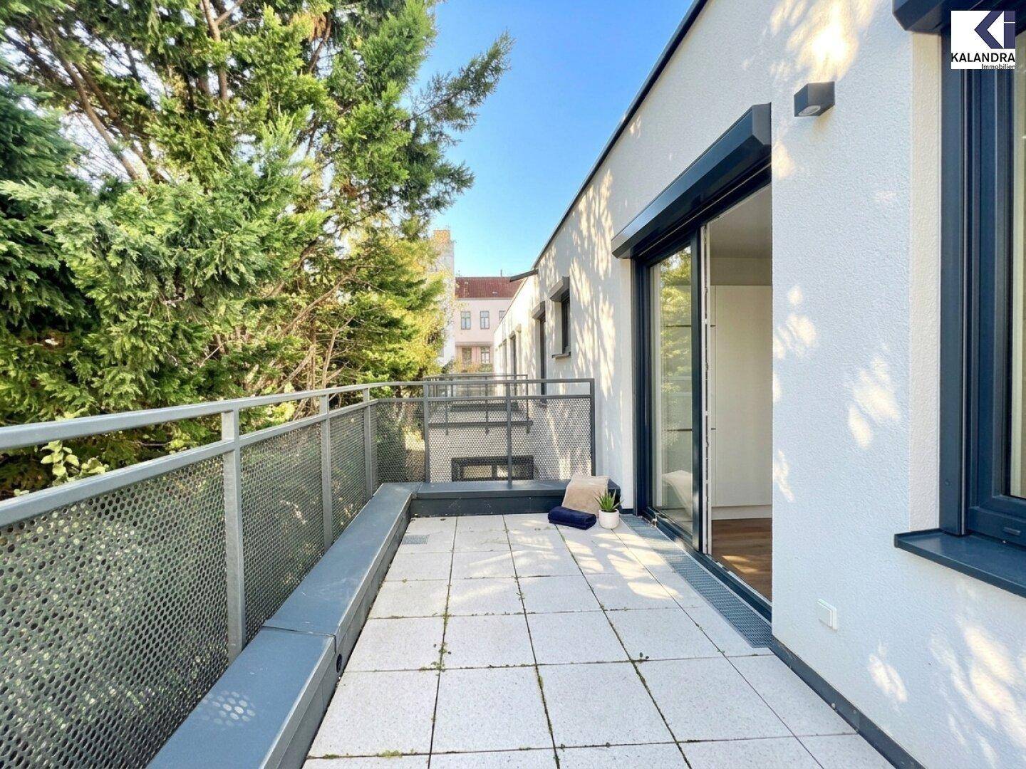 Helle Terrasse mit Zugang zu den Innenräumen, umgeben von üppigem Grün und mit Blick auf die Umgebung.