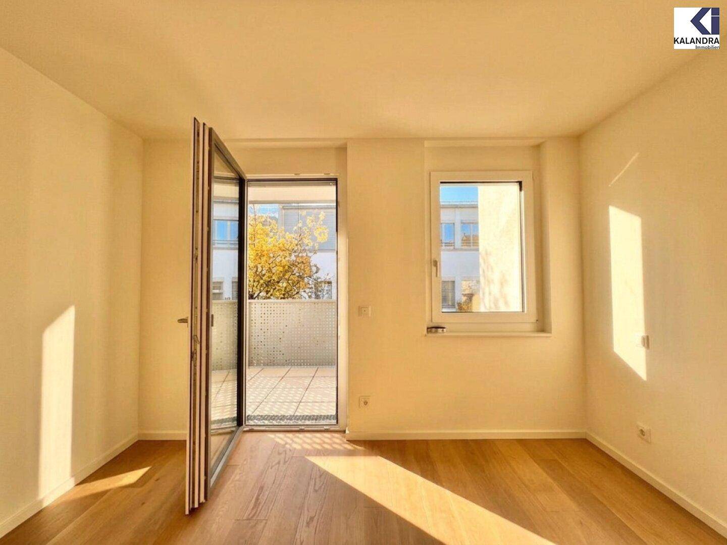 Lichtdurchfluteter Raum mit Holzboden und Zugang zu einem sonnigen Balkon.