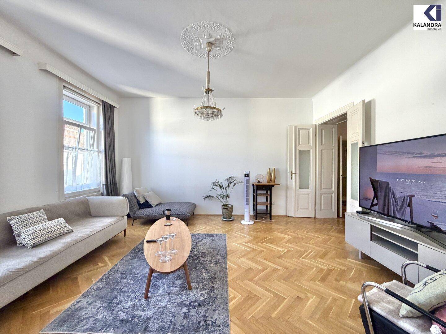 Weitläufiges Wohnzimmer mit Fischgrätparkett, modernem Mobiliar und dekorativer Deckenrosette.