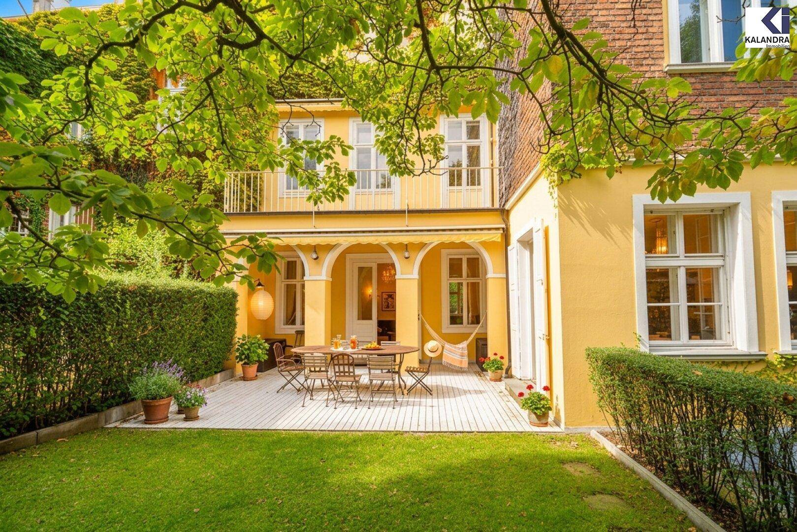 Charmante Holzterrasse mit Gartenmöbeln und Markise, umgeben von einem grünen Garten und der gelben Villa.