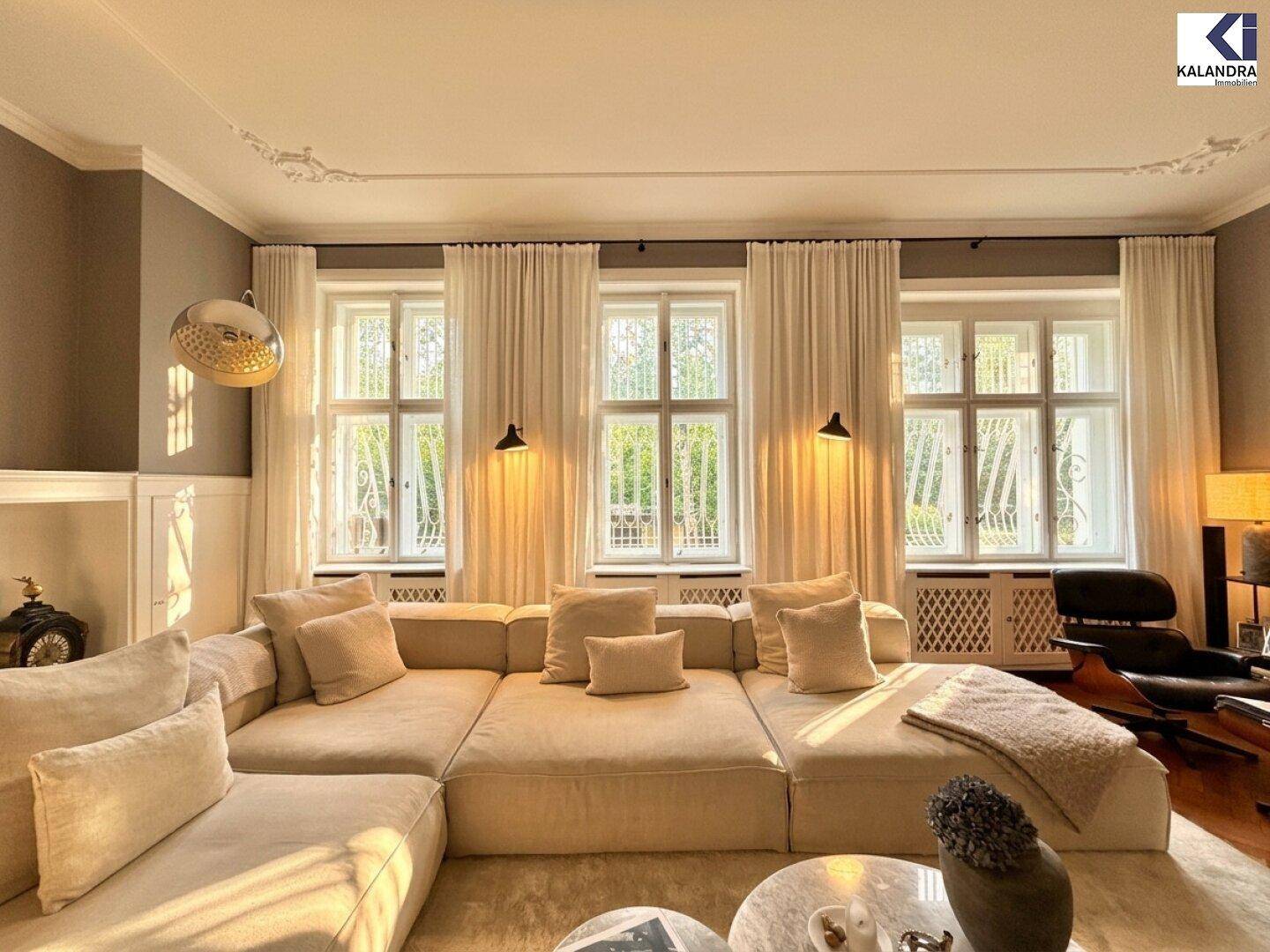 Geräumiges Wohnzimmer mit großem Ecksofa, vielen Fenstern und elegantem Parkettboden, hell und sonnig.