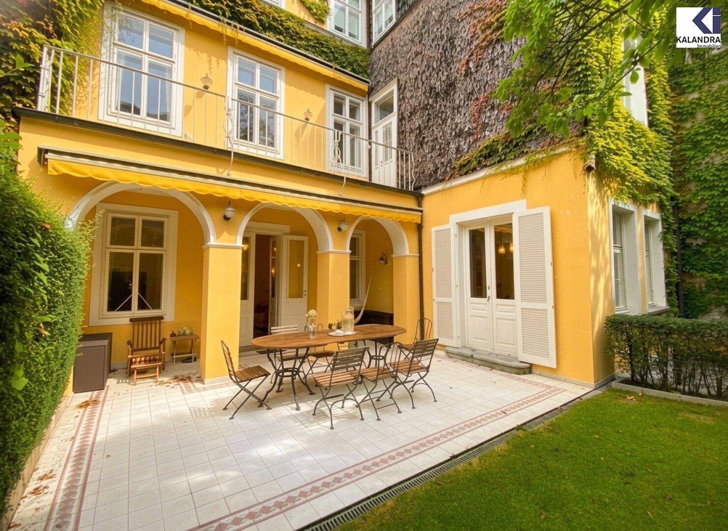 Große geflieste Terrasse mit Gartenmöbeln und Markise, umgeben von einem gepflegten Garten und der Villa.
