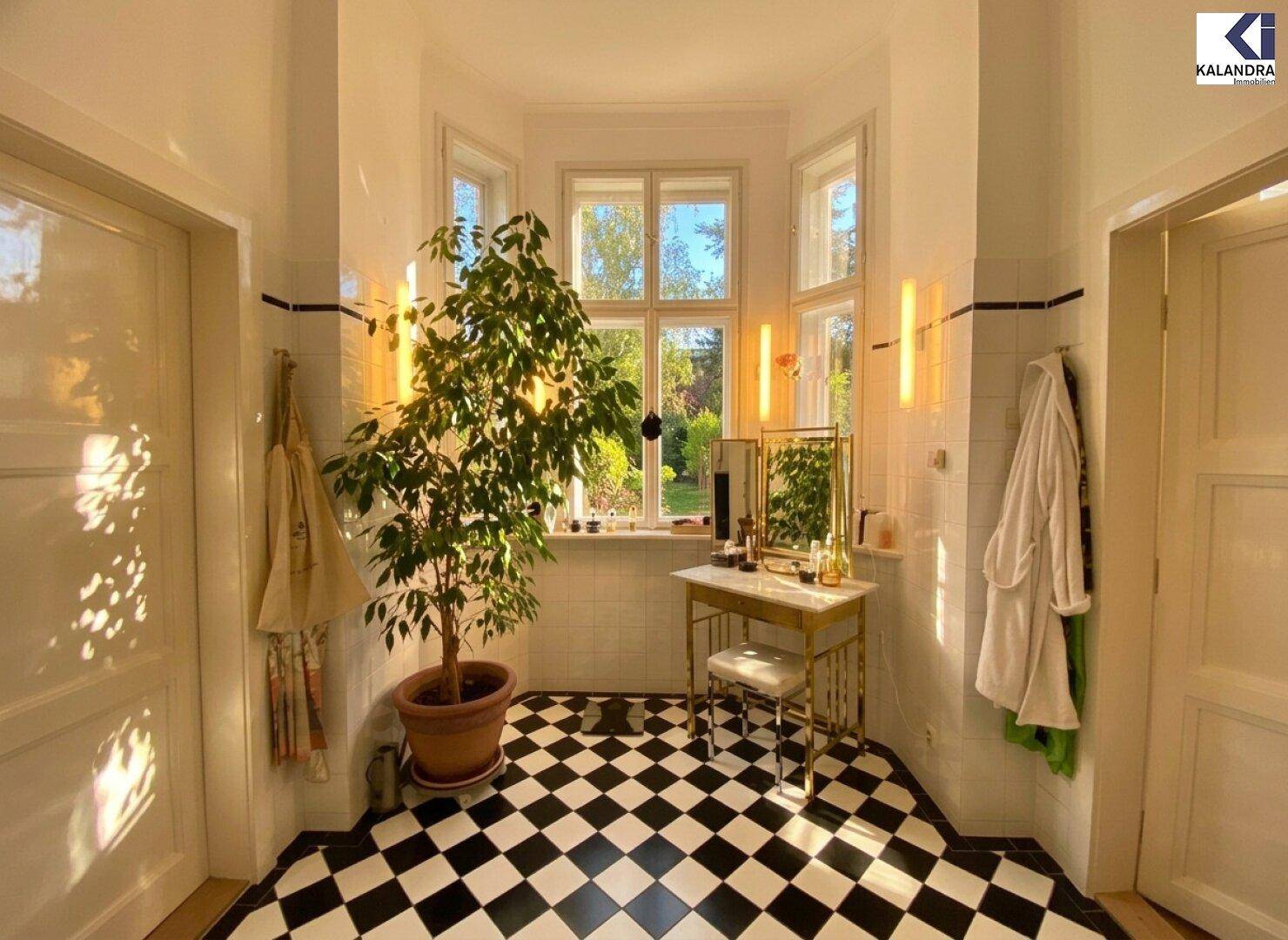 Helles Badezimmer mit markanten schwarz-weißen Schachbrettfliesen, Schminktisch und großen Fenstern.