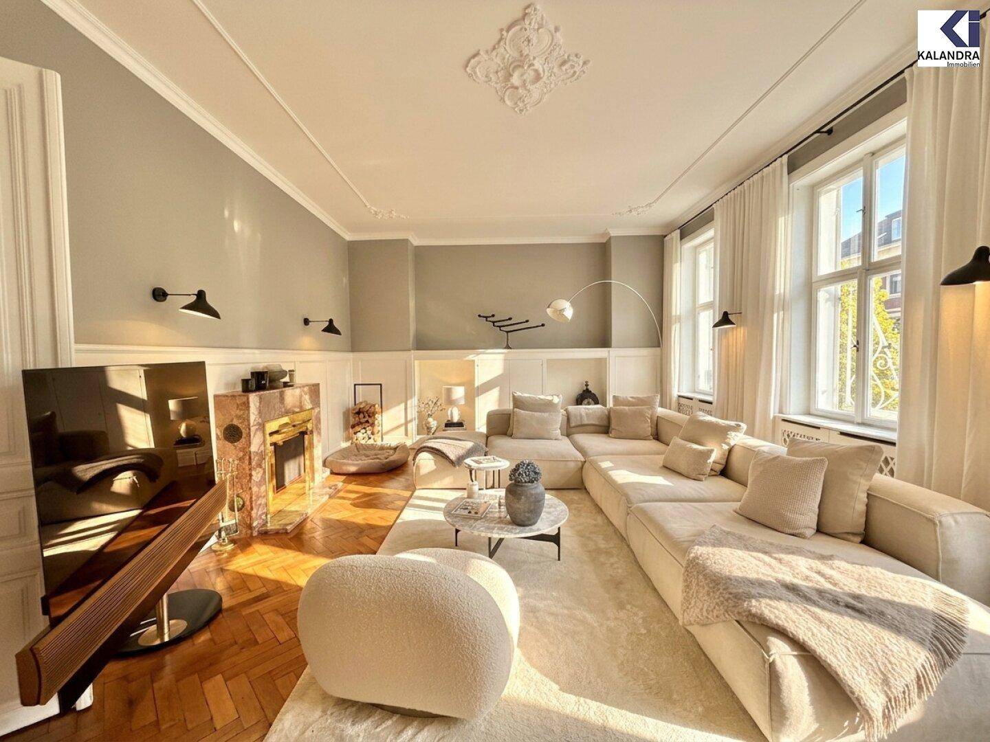 Elegantes Wohnzimmer mit großem Sofa, Kamin, Fischgrätparkett und hohen Decken mit Stuckverzierung.