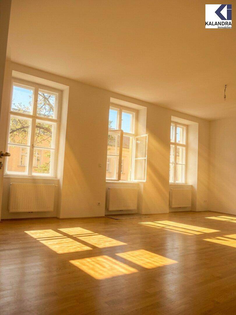 Lichtdurchflutetes Wohnzimmer mit Parkettboden und mehreren Fenstern, die einen Blick nach draußen bieten.