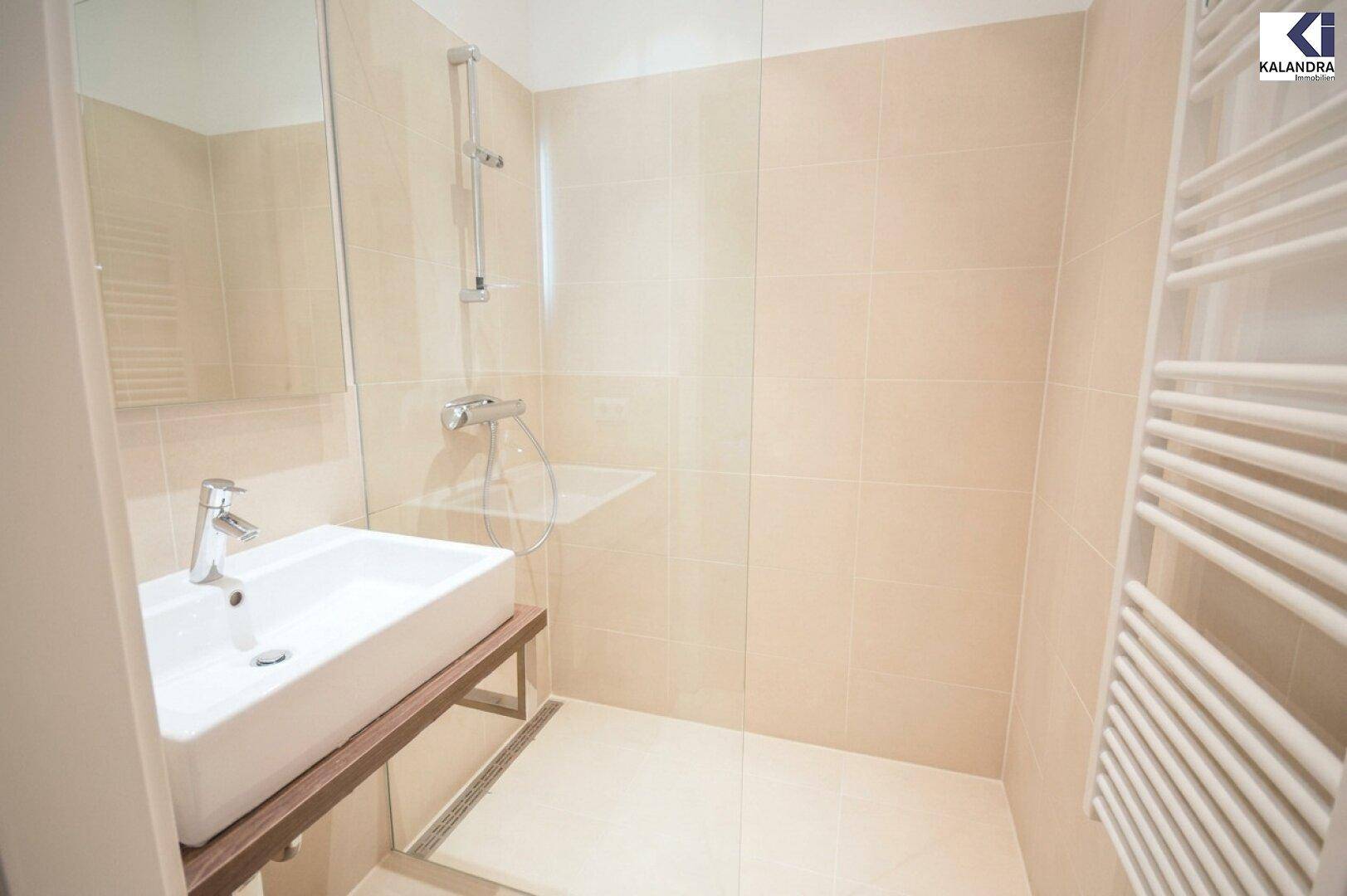 Modernes Badezimmer mit beigefarbenen Fliesen, ebenerdiger Dusche und Handtuchheizkörper.