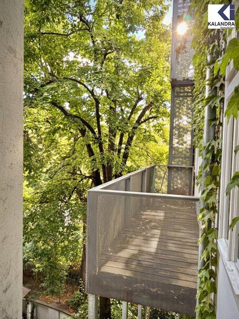 Heller Balkon mit Metallgeländer und Blick ins Grüne, umgeben von Bäumen.