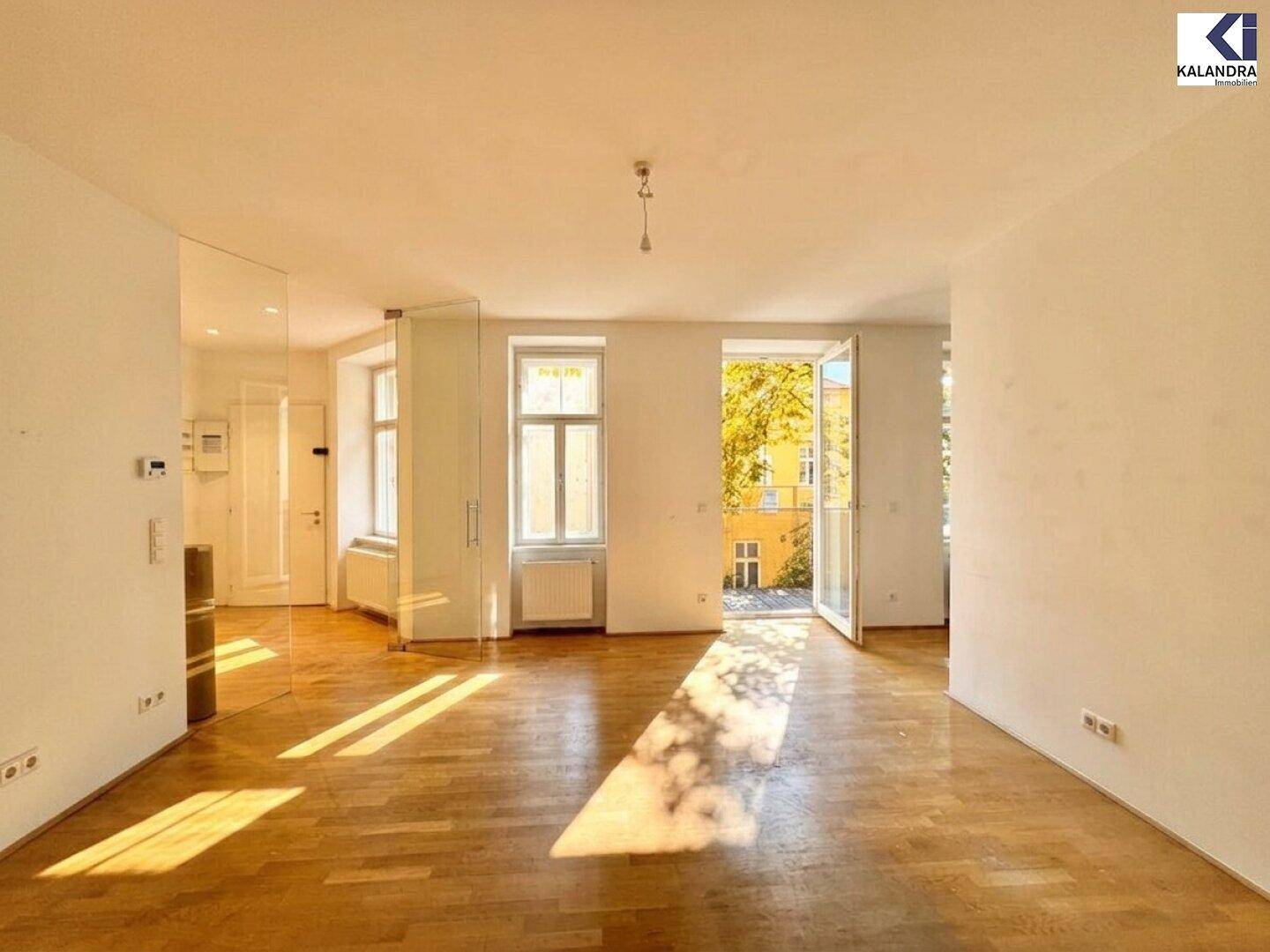 Heller Wohnraum mit Parkettboden und Zugang zu einem Balkon, durchflutet von Sonnenlicht.
