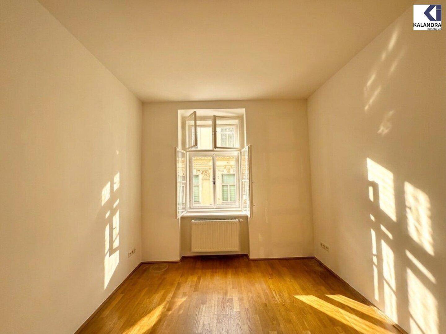 Ruhiges Zimmer mit Parkettboden und einem Fenster, das Sonnenlicht auf den Boden wirft.