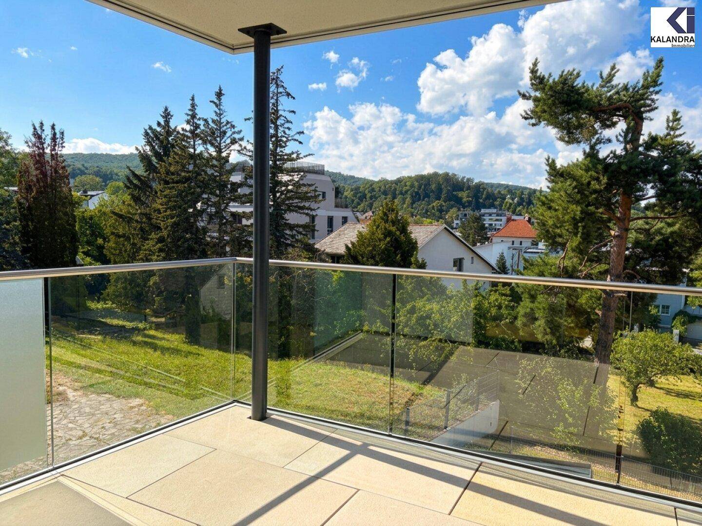 Balkon mit Glasgeländer und weitem Blick auf bewaldete Hügel und die umliegende Landschaft.