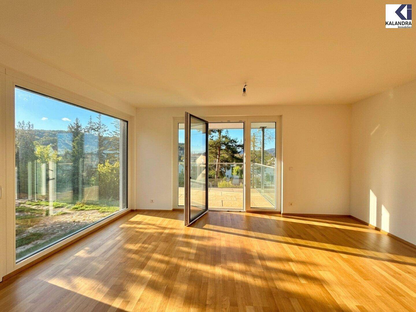 Helles Wohnzimmer mit großen Fenstern, Holzboden und Zugang zu einem Außenbereich.