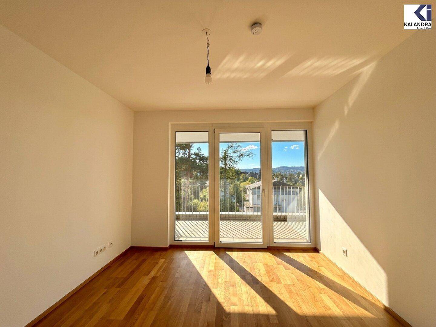 Heller Raum mit Holzboden und Zugang zu einem Balkon mit weitem Ausblick.