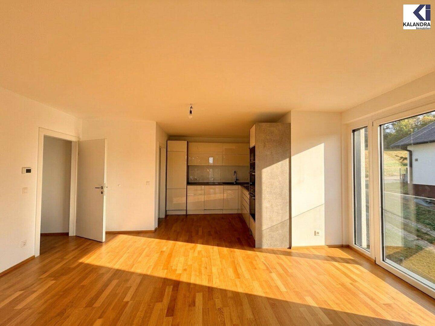 Offener Wohnbereich mit integrierter Küchenzeile und viel Tageslicht durch große Fenster.