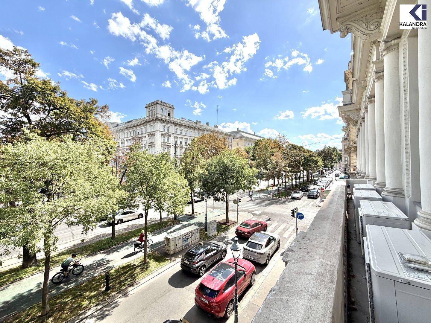 Balkon mit weitem Blick auf eine belebte Stadtstraße, gesäumt von Bäumen und historischen Gebäuden.