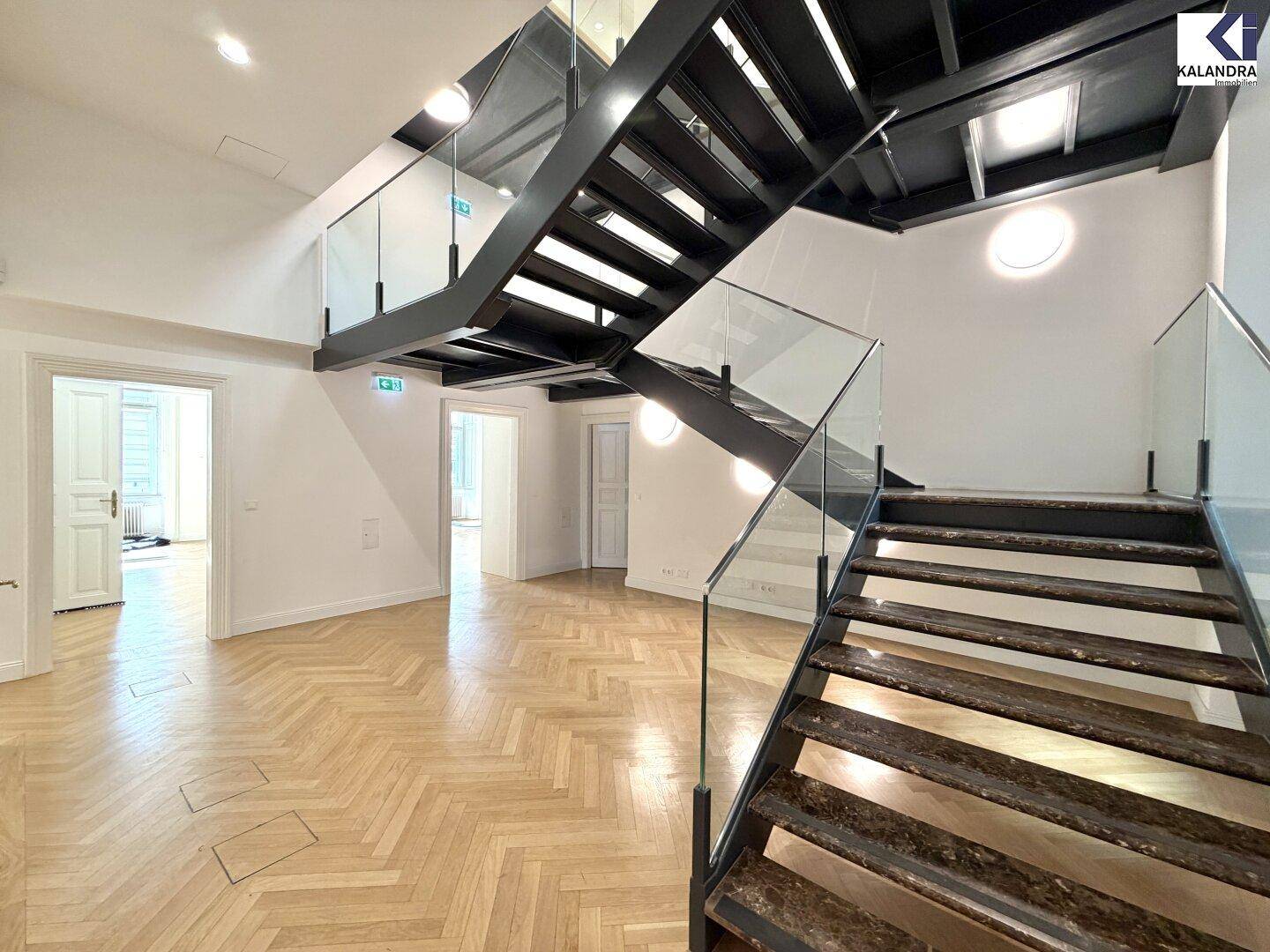 Moderner Eingangsbereich mit Holzparkett und einer eleganten Treppe mit Glasgeländer, die in die oberen Etagen führt.