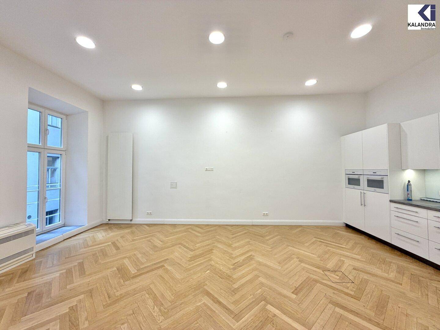 Moderne, helle Küche mit weißen Hochglanzschränken, integrierten Geräten und Fischgrätparkett.