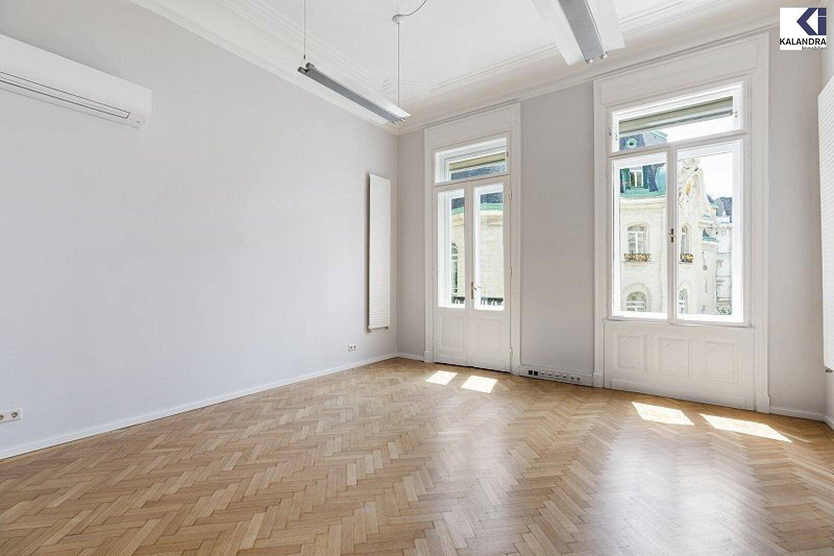 Geräumiges Zimmer mit Fischgrätparkett, hohen Decken, Klimaanlage und zwei großen Fenstern mit Stadtblick.