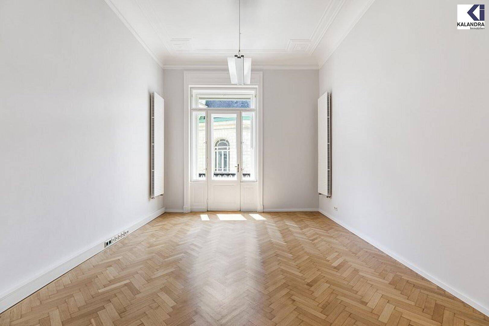 Symmetrischer Raum mit hellem Fischgrätparkett, hohen Decken und einem großen Fenster, das viel Licht hereinlässt.