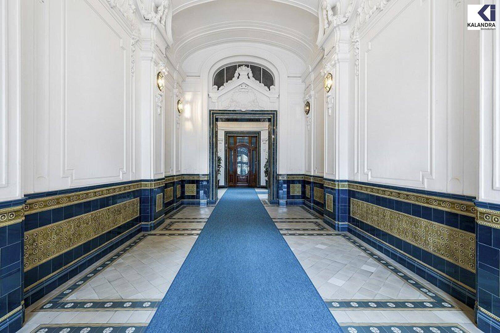 Prunkvoller Flur mit blauem Teppichläufer, verzierten Wänden und einer eleganten Gewölbedecke.