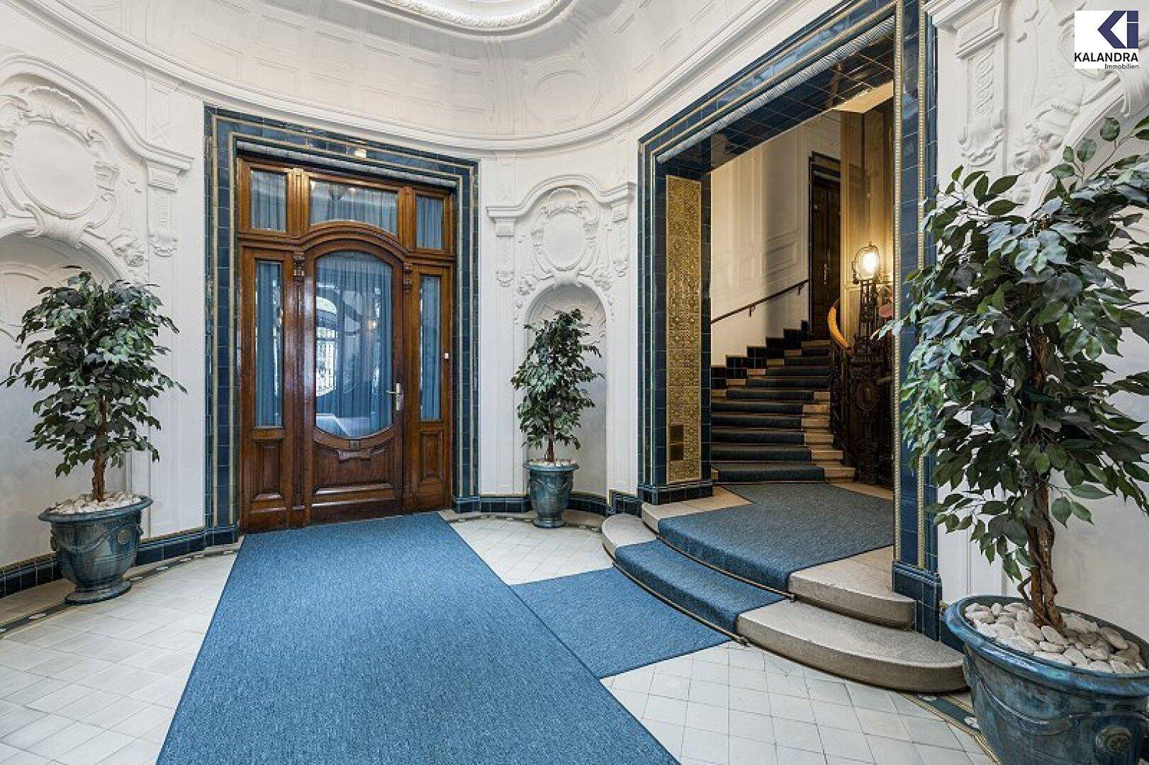 Repräsentativer Eingangsbereich mit einer kunstvollen Holztür, Topfpflanzen und einer eleganten Treppe im Hintergrund.