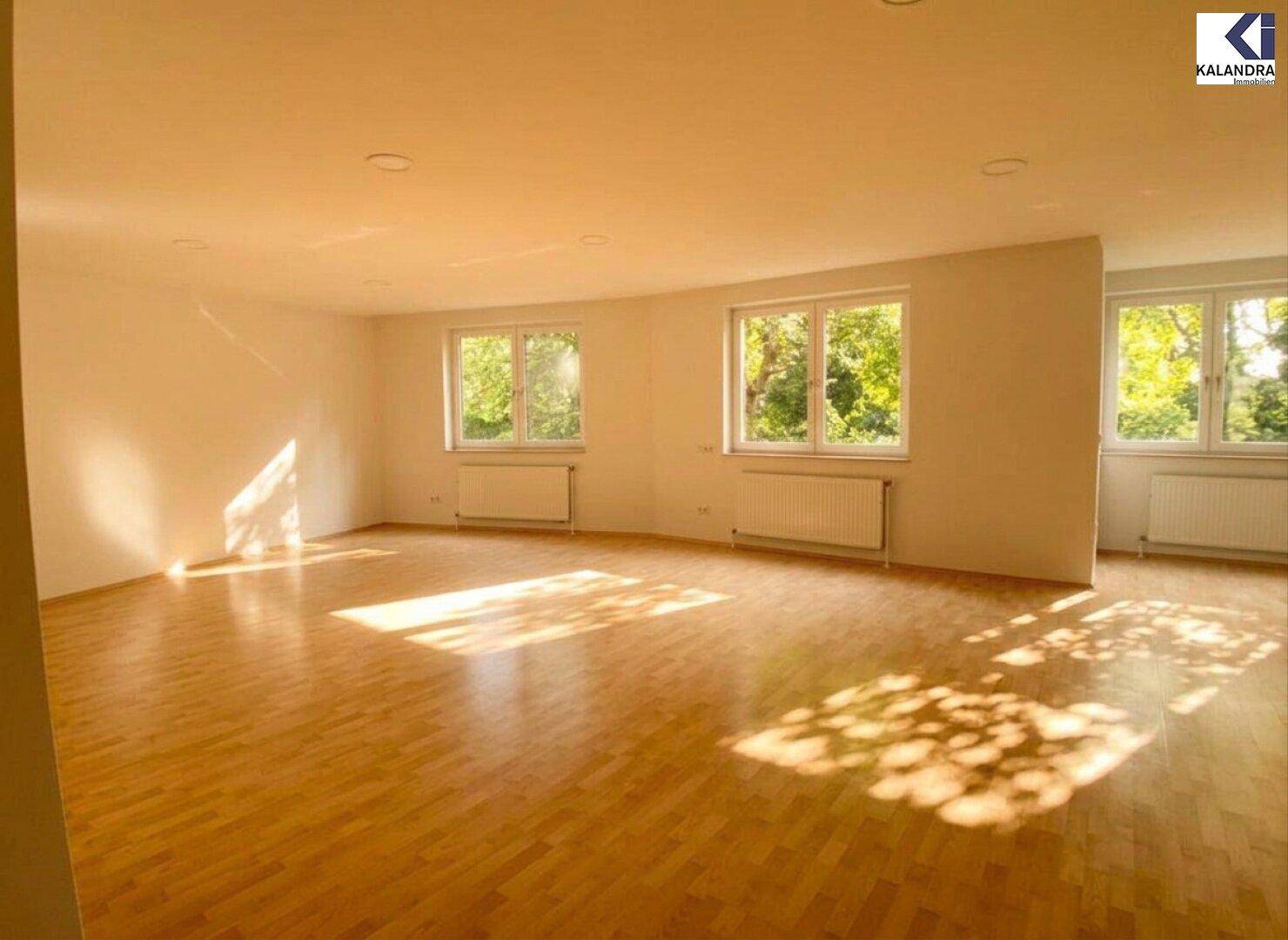 Heller Wohnbereich mit Parkettboden und mehreren Fenstern, die viel Sonnenlicht hereinlassen.