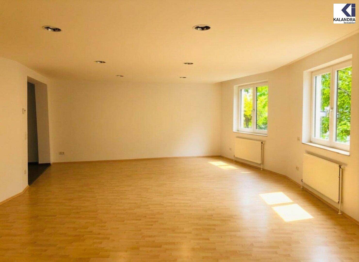 Geräumiger Wohnbereich mit Parkettboden, Einbaustrahlern und Fenstern mit Blick ins Grüne.
